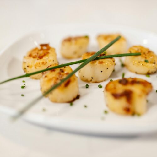 Crispy lion's mane mushroom "scallops" garnished with fresh parsley on a white plate.